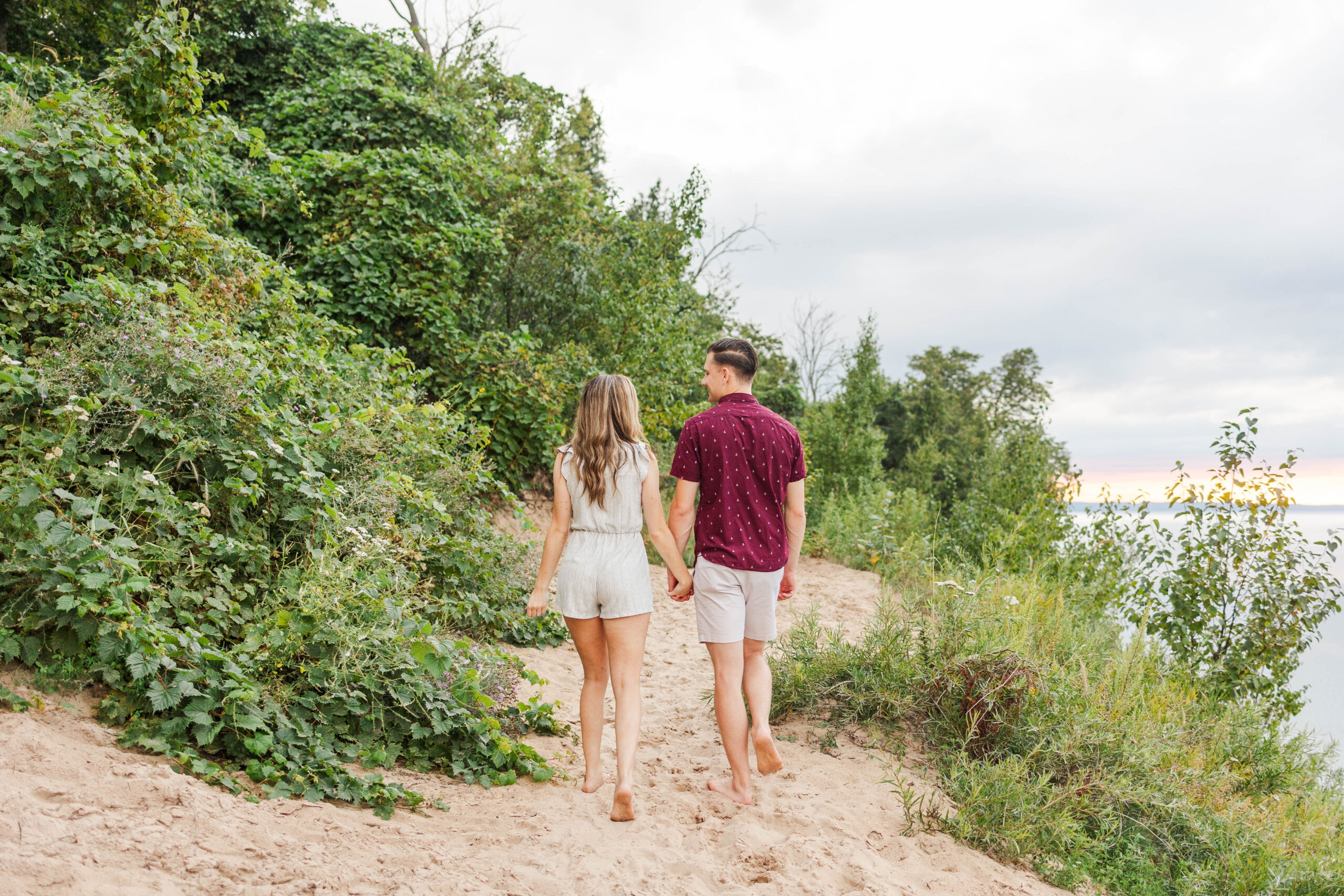 Couple walking barefoot on the sandy trail at Pyramid Point in Northern Michigan after their surprise proposal