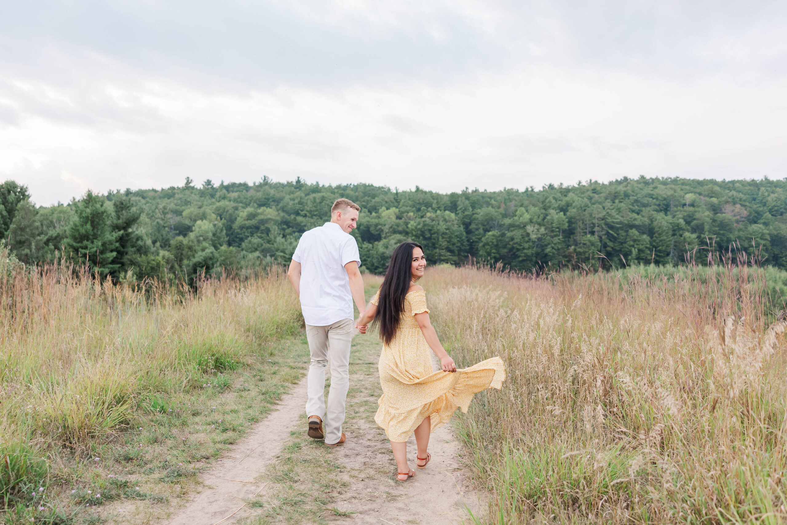 Engaged couple walking hand in hand through a meadow at Brown Bridge in Kingsley, MI during their Traverse City engagement session