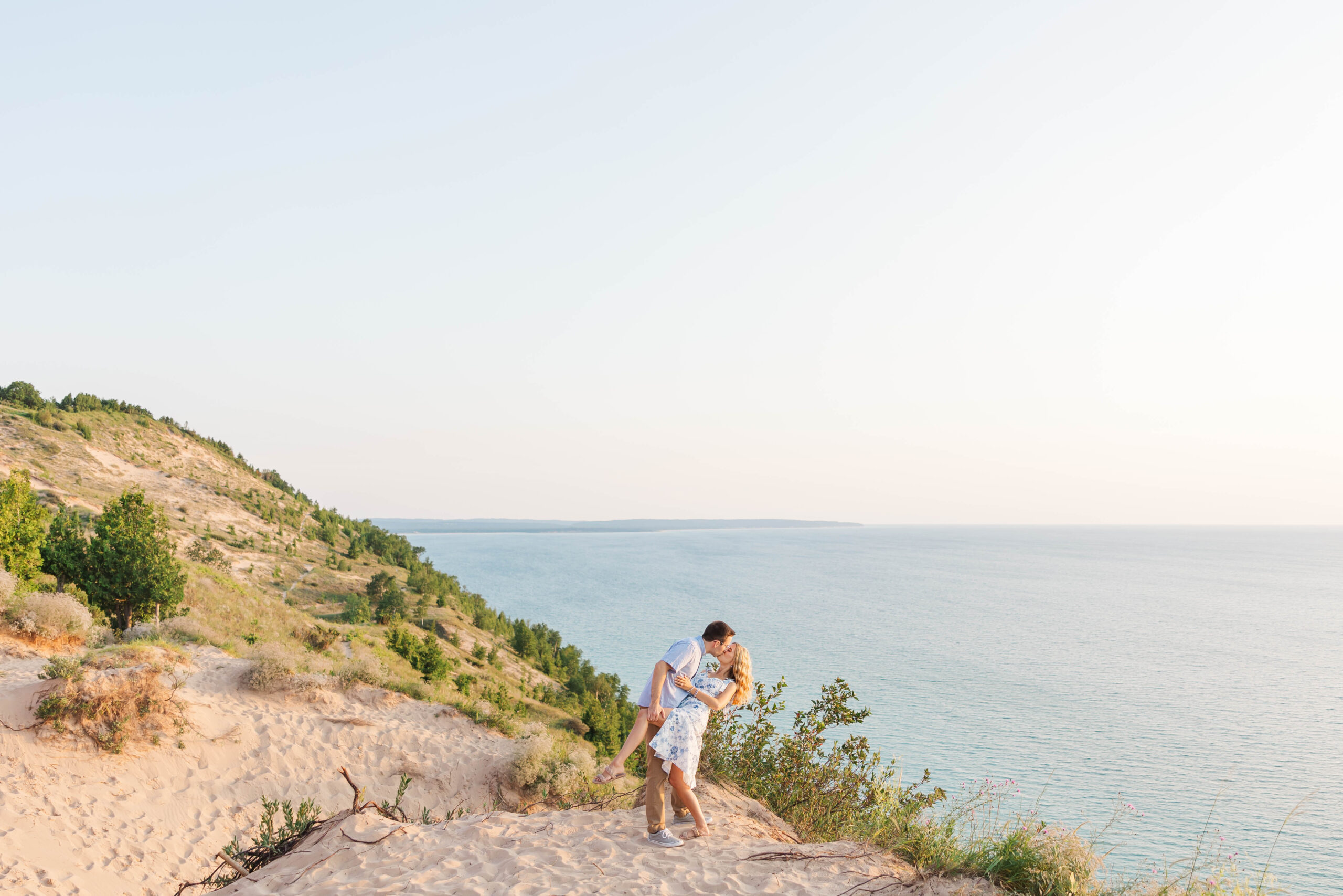 Couple sharing a kiss on the edge of Empire Bluff with sweeping views of Sleeping Bear Dunes and Lake Michigan at sunset
