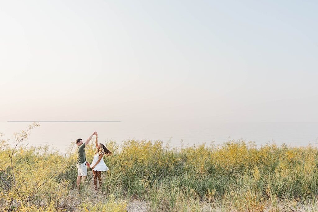 Candid Northern Michigan beach engagement photos capturing a joyful couple by the water