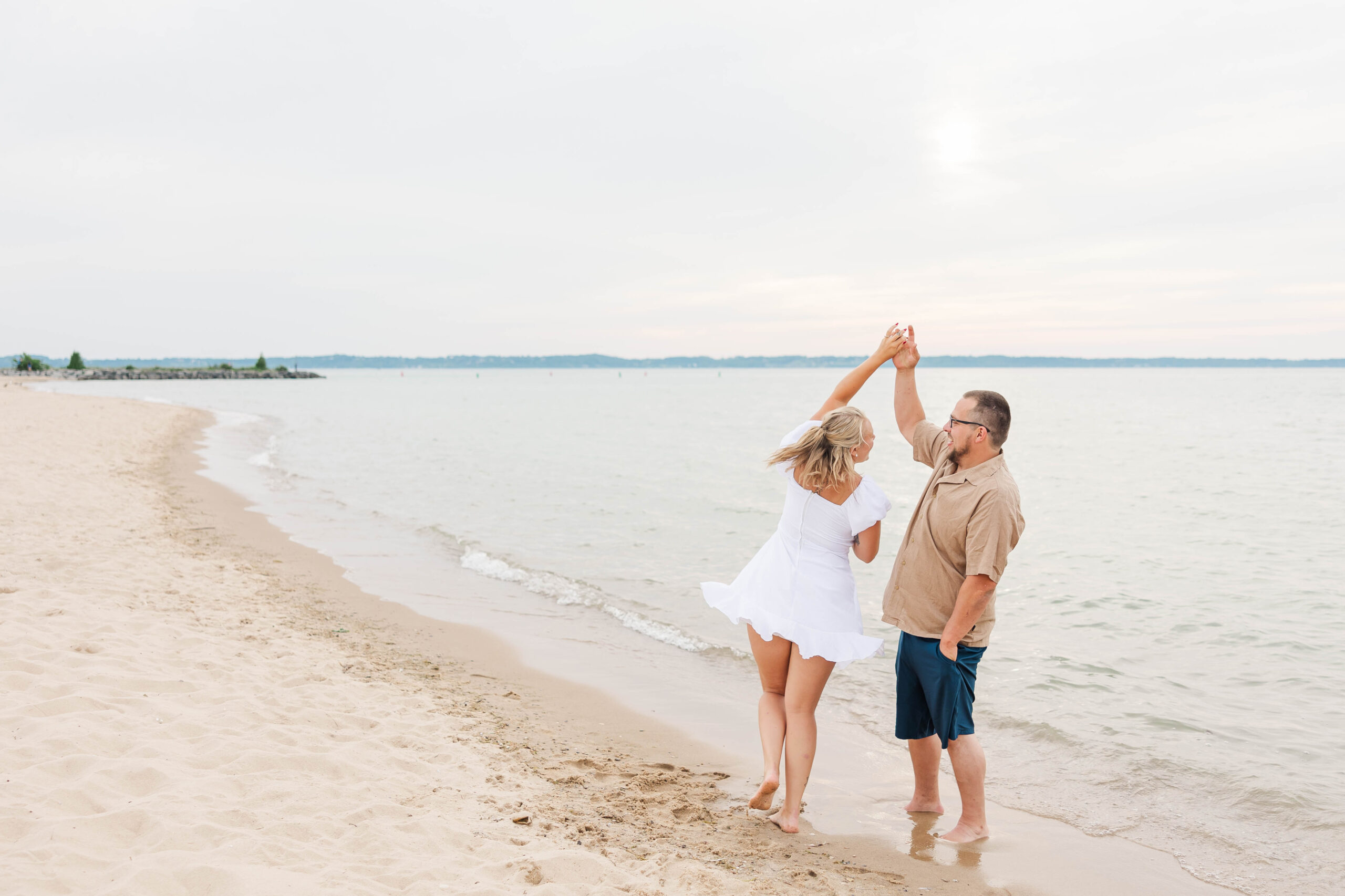 Engaged couple embracing on the beach at The Dam Beach in Elk Rapids, Michigan during their romantic Northern Michigan engagement session
