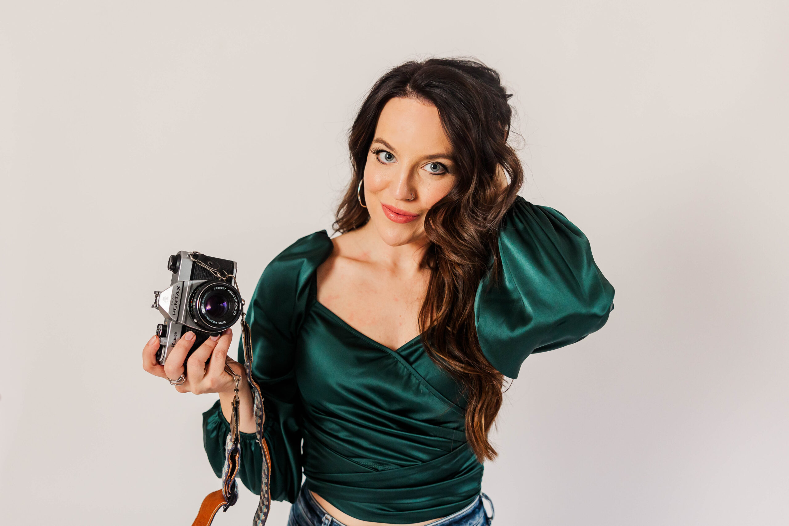 Female photographer in emerald green top holding vintage camera during editorial branding session in Traverse City studio