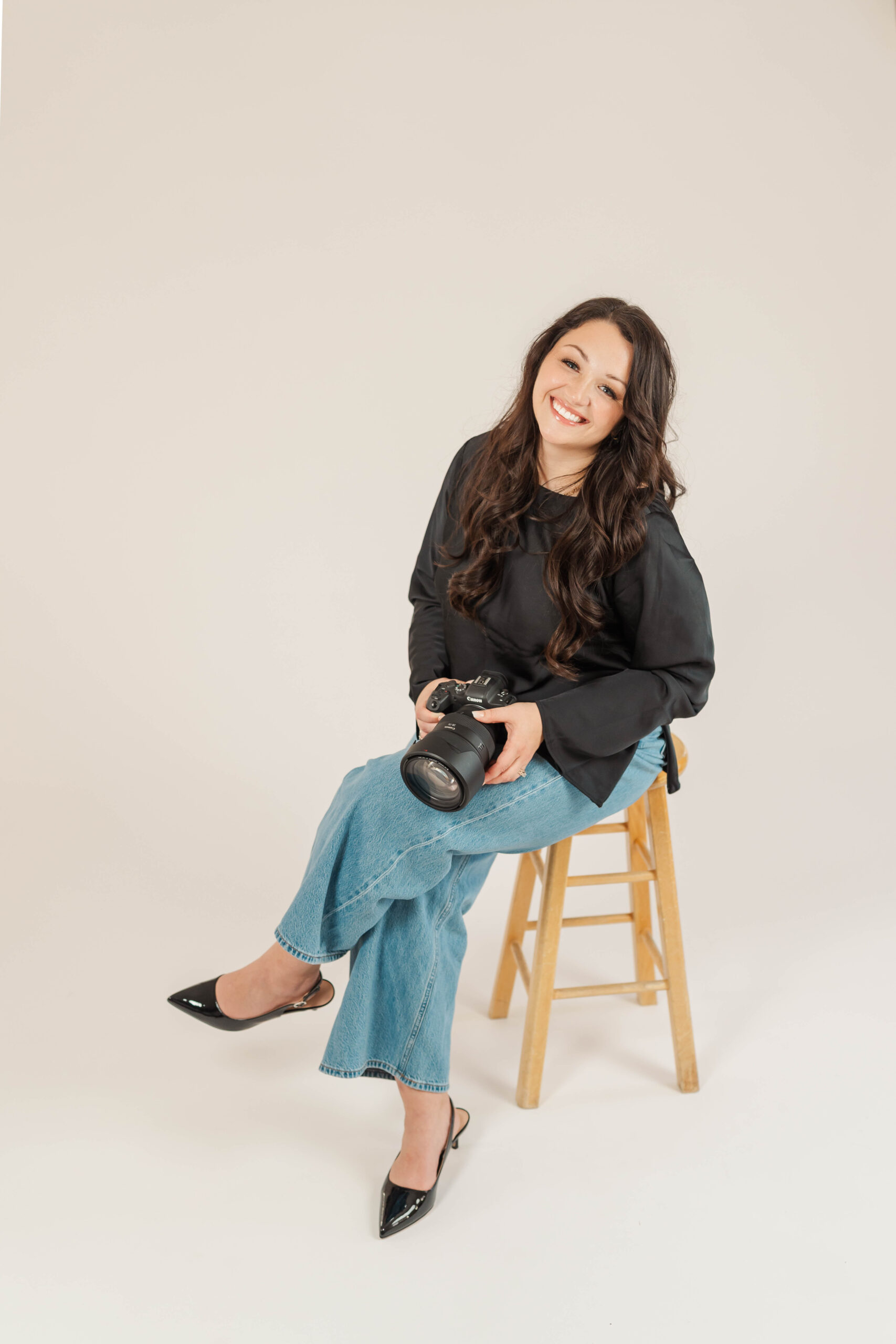 Photographer sitting on a stool holding a camera, smiling — Northern Michigan wedding and family photographer branding photo