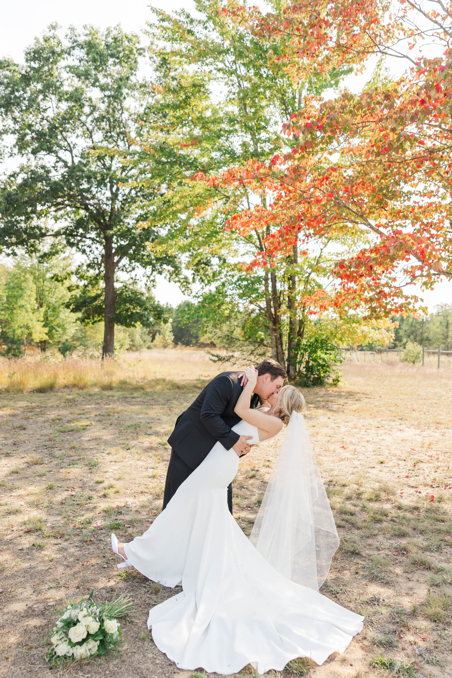 Bride and groom sharing a kiss under colorful fall trees at The Mill Pond Event Center in Kalkaska, Michigan