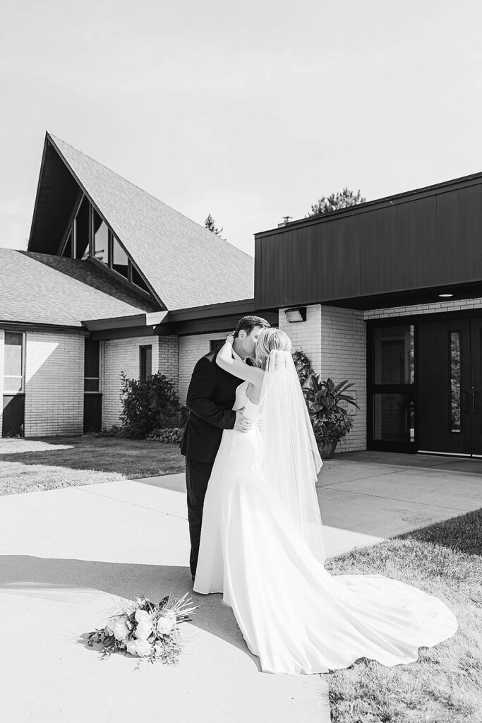 Black and white portrait of bride and groom kissing outside their Catholic wedding church