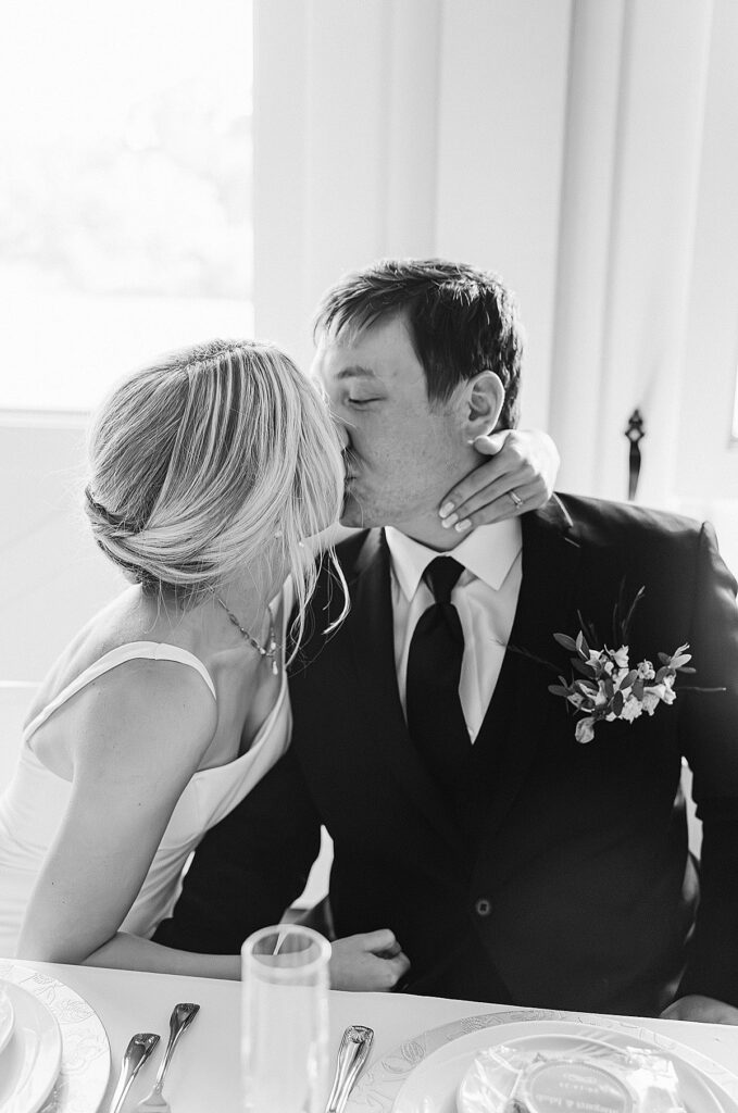 Black and white photo of bride and groom kissing at their wedding head table