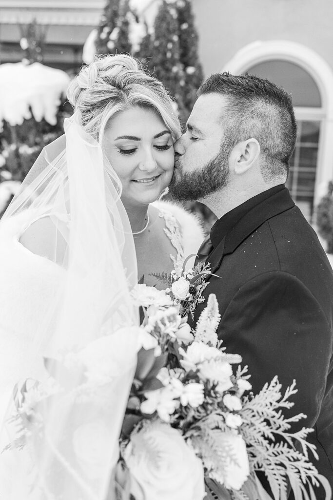 Bride and groom embracing during snowy winter wedding portraits