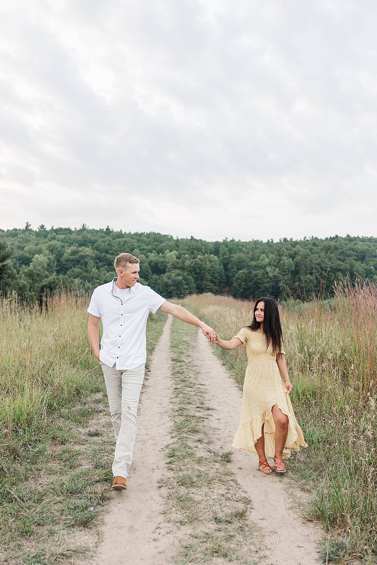 Couple walking hand in hand during a Northern Michigan engagement session on a scenic trail