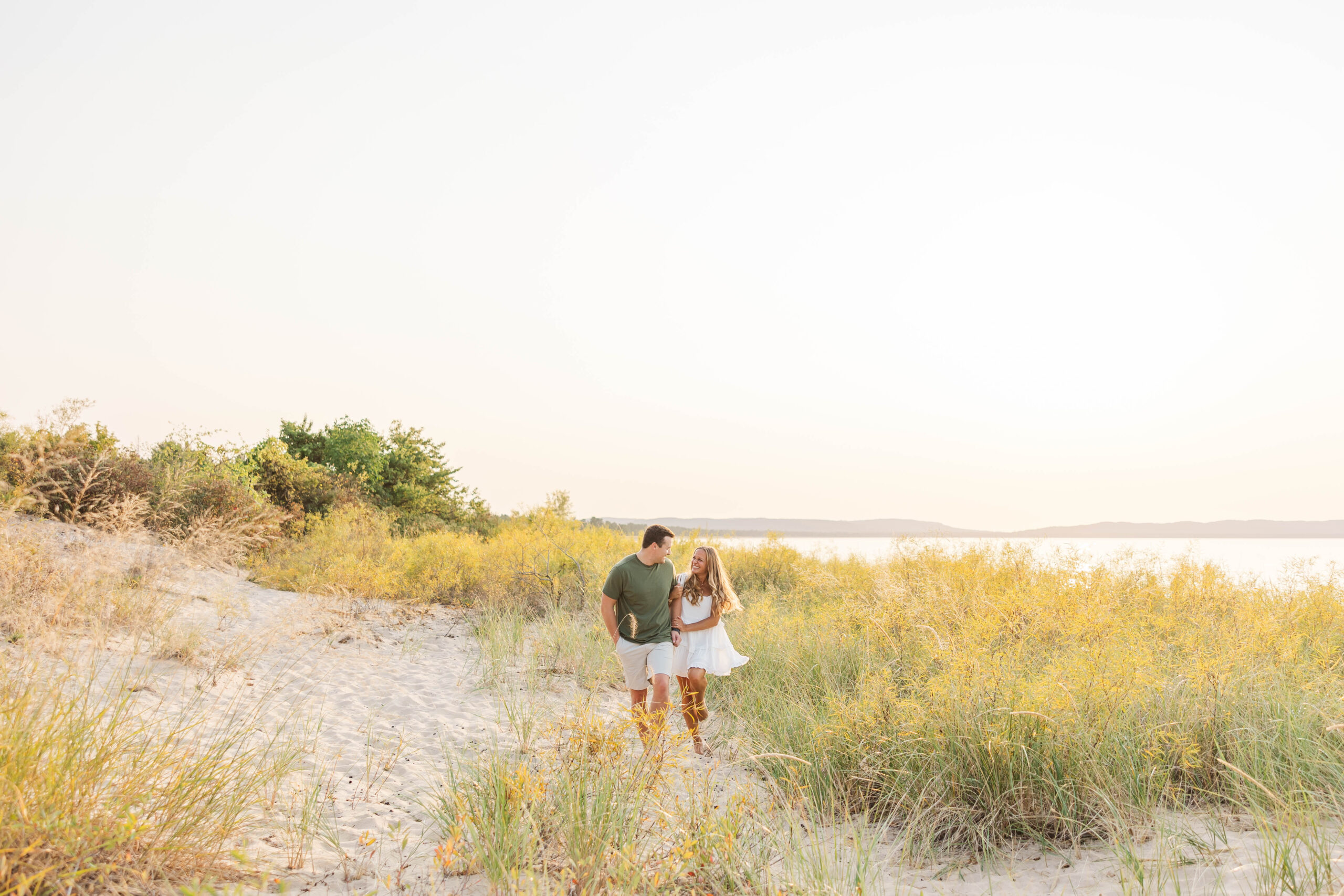Engaged couple walking together along sand dunes at Good Harbor Beach near Traverse City, Michigan during sunset