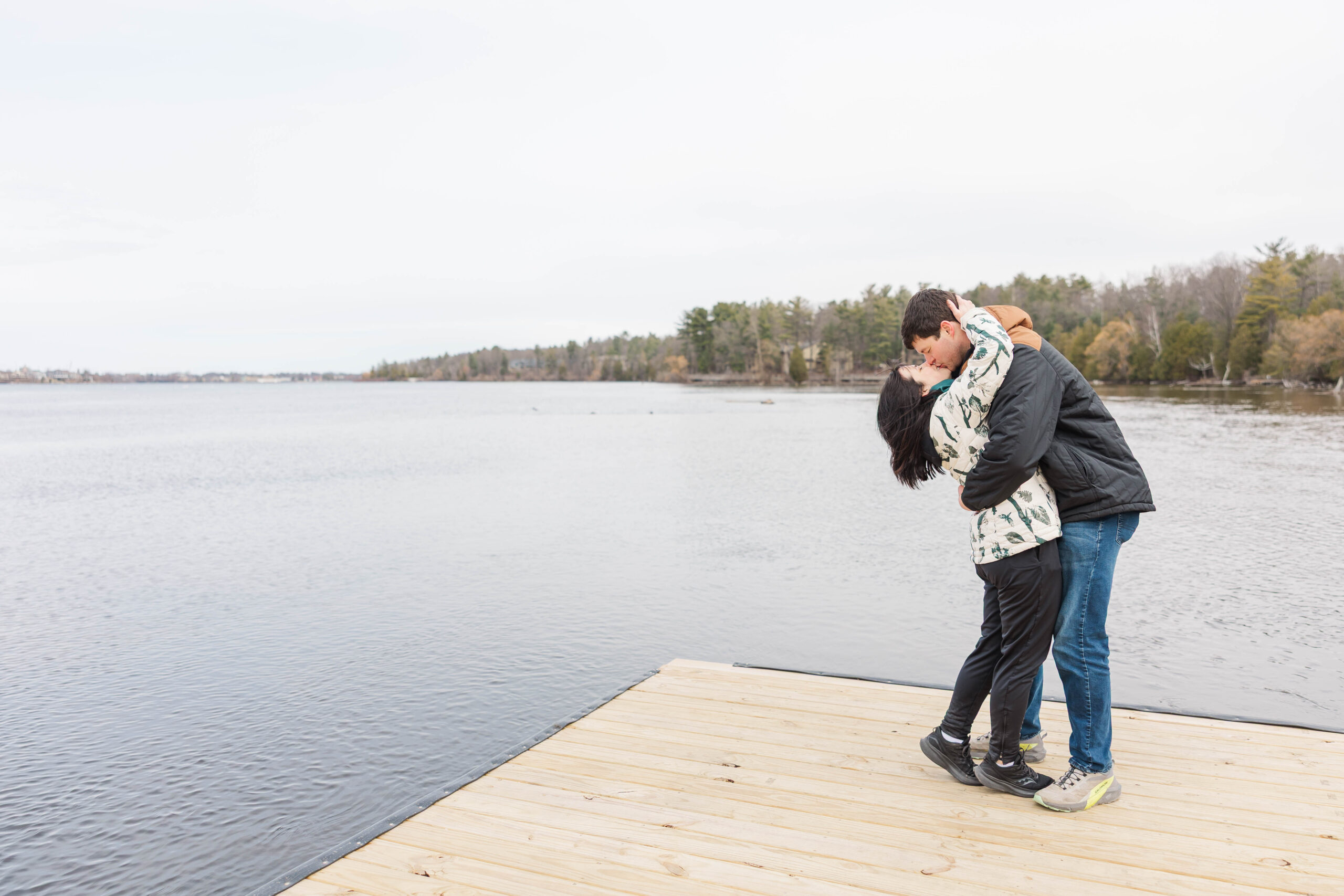 Couple sharing a joyful kiss on the dock after a proposal on the Boardman Lake Trail in Northern Michigan