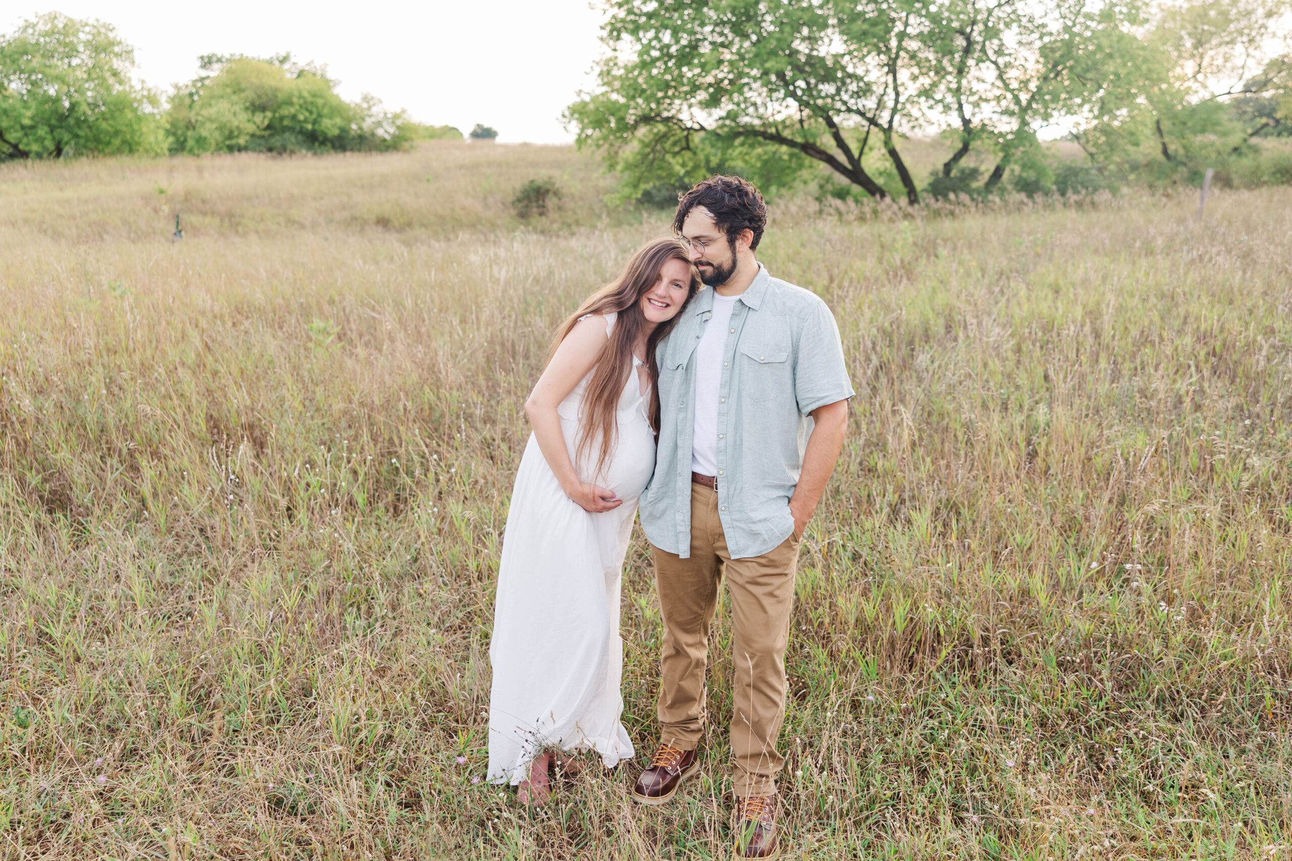 Expecting couple sharing a joyful moment in a grassy field during their maternity session at the Botanical Gardens in Traverse City, Michigan