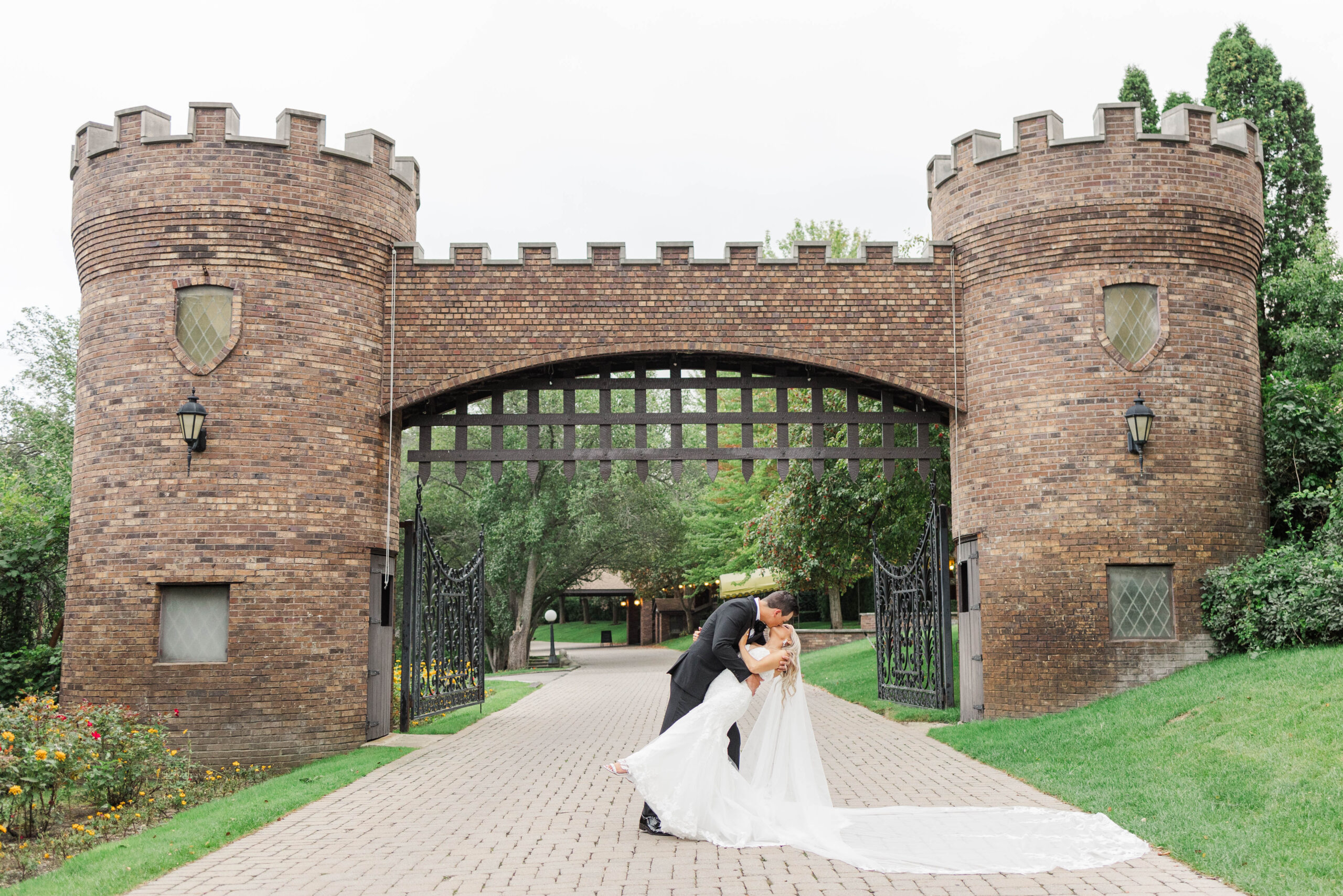 Bride and groom kissing beneath the iconic castle gate at Greencrest Manor, a romantic Michigan wedding venue