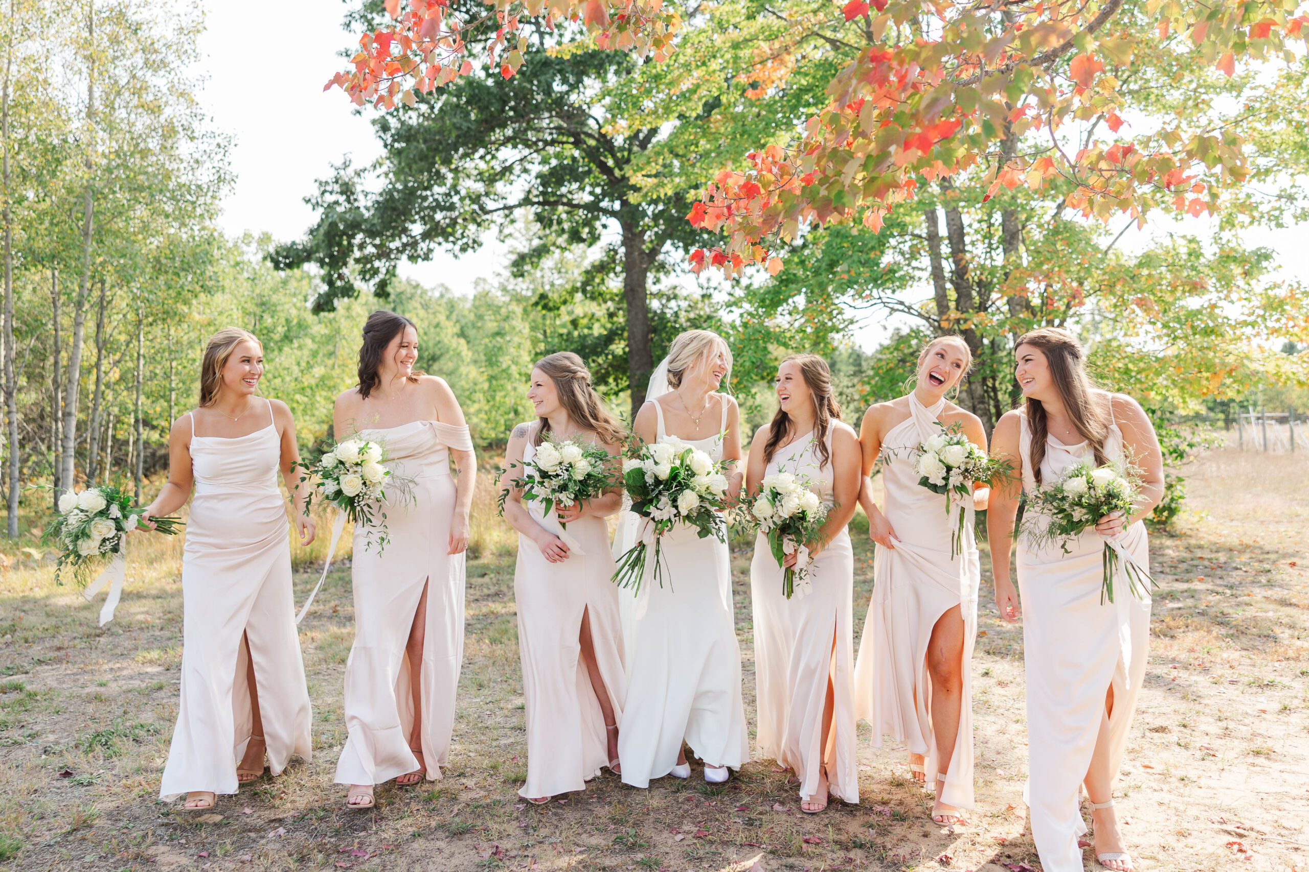 Bride laughing with her bridesmaids in soft neutral dresses at a Northern Michigan wedding venue surrounded by fall colors