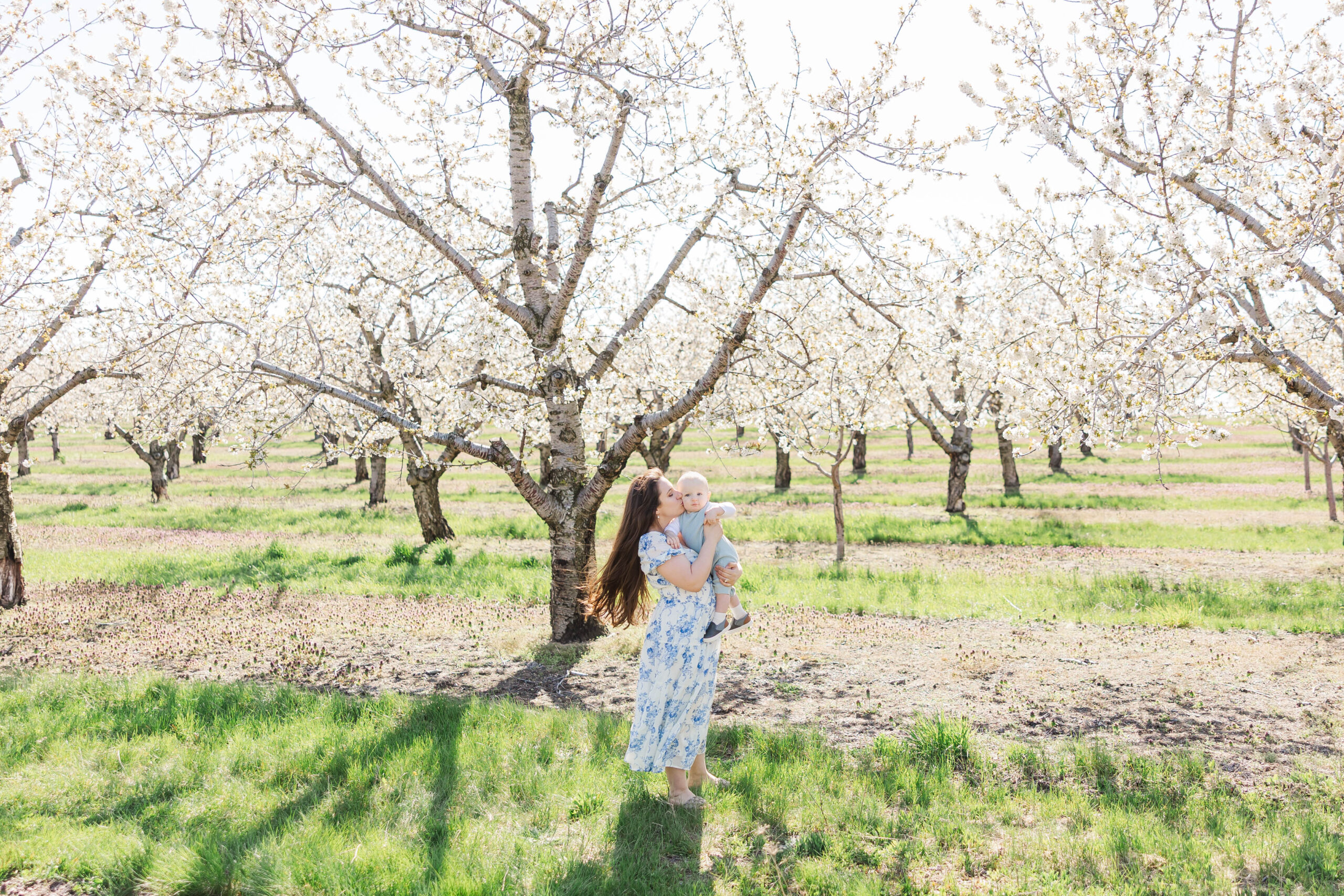 Mother holding her baby in a blooming cherry orchard during a spring family session in Northern Michigan