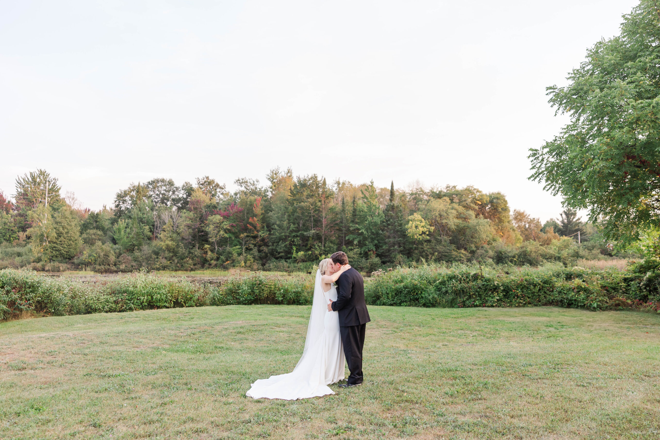 Bride and groom sharing a kiss in a peaceful Northern Michigan garden surrounded by trees and open fields