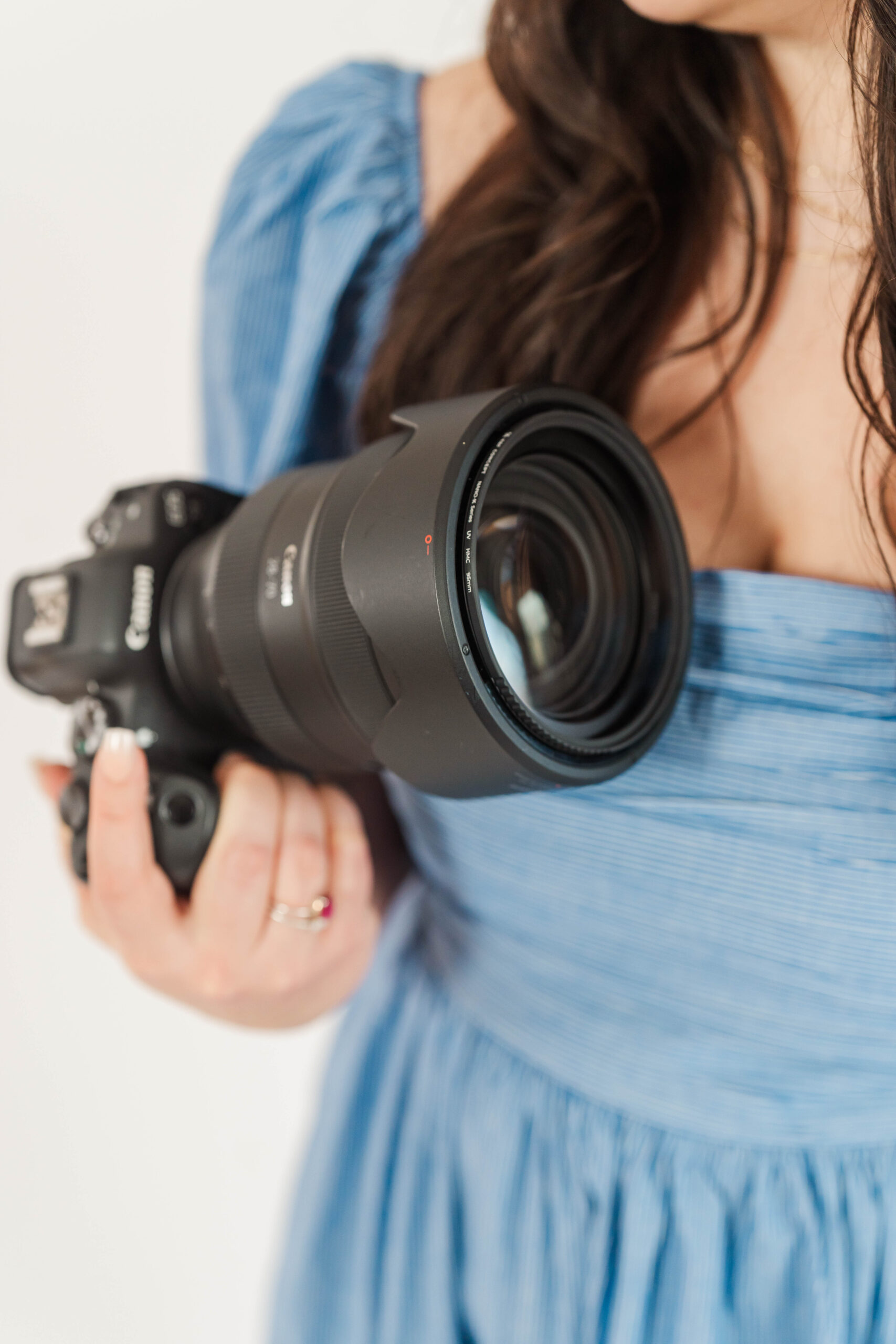 Close-up of a photographer holding a Canon camera with a large lens, perfect for learning manual mode settings like ISO, aperture, and shutter speed