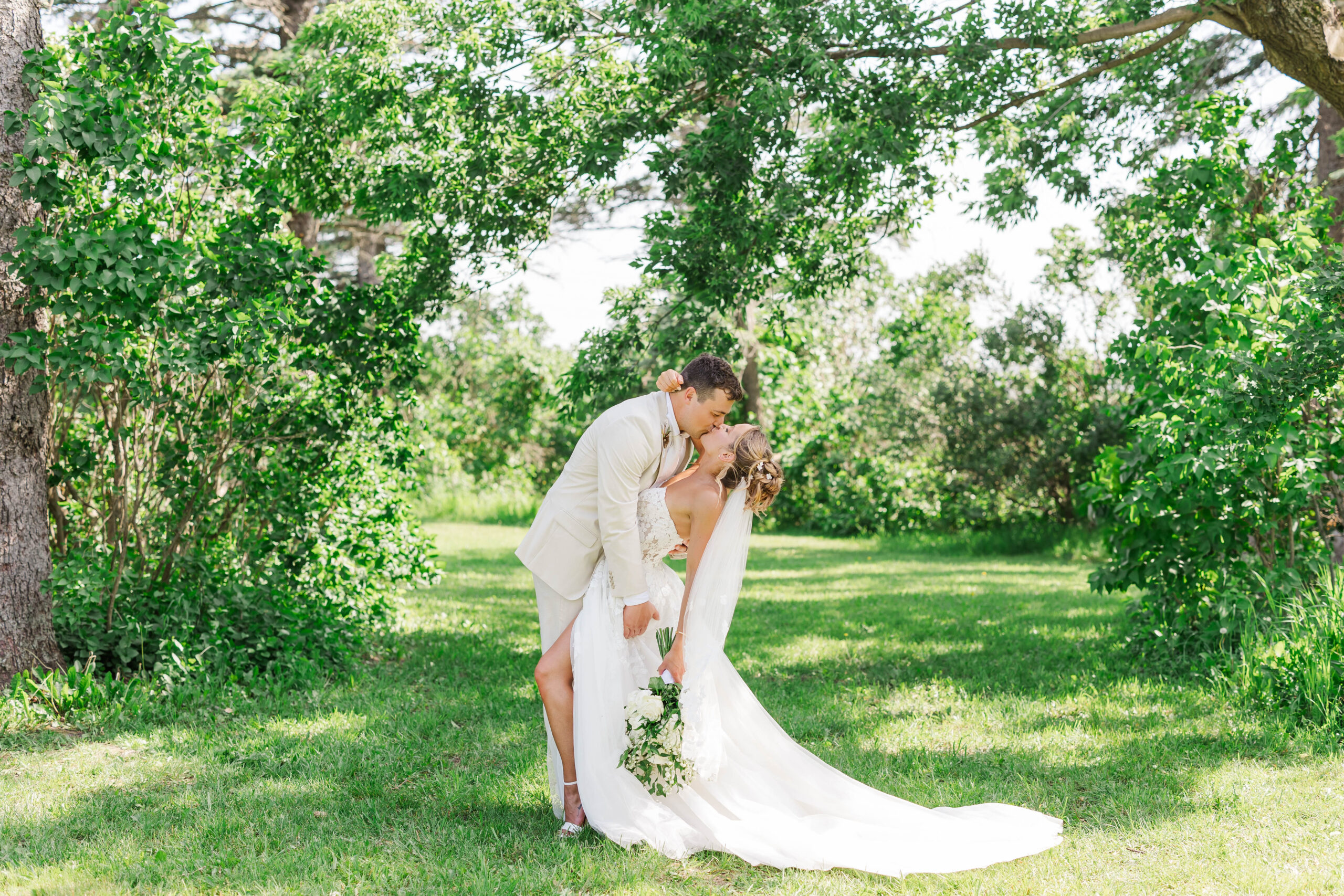 Groom dipping bride for a kiss in a sunny Northern Michigan outdoor wedding.