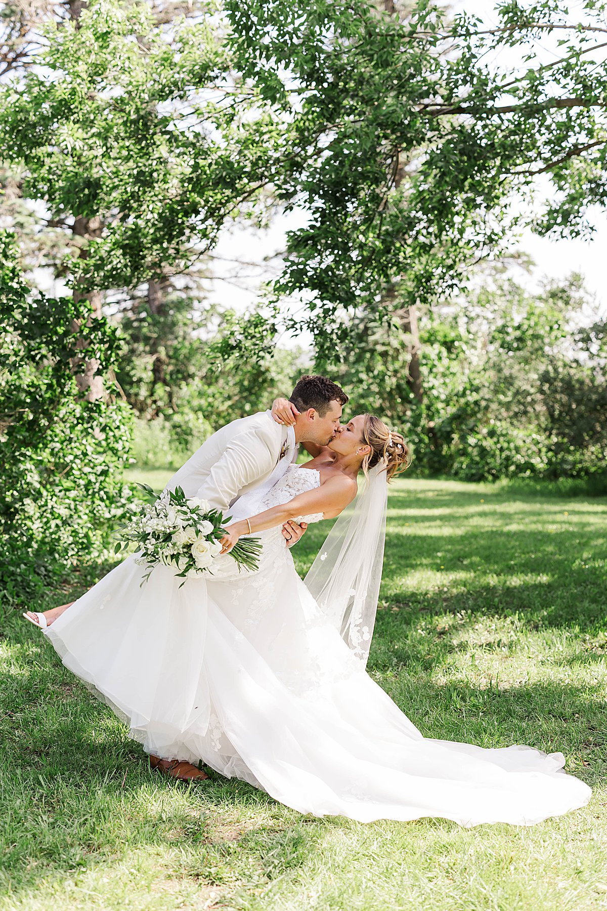 Bride and groom sharing a romantic dip kiss under the trees at Blue Sky Barn in Elmira, Michigan