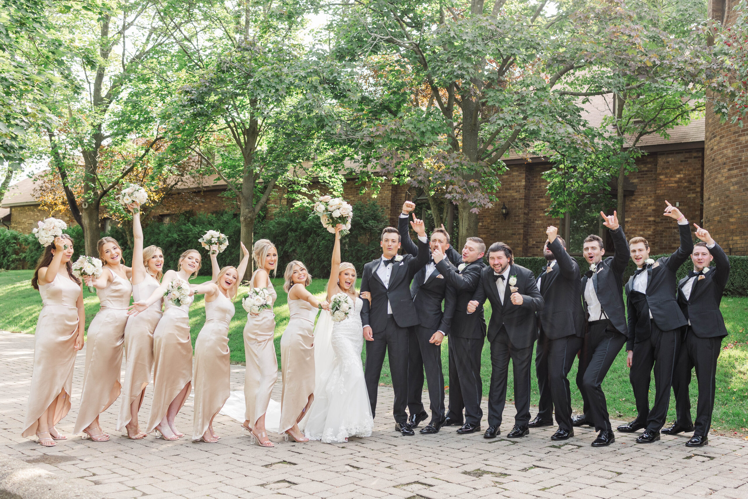 Bride and groom celebrating with their bridal party in champagne dresses and black tuxedos at Indianwood Country Club in Lake Orion, Michigan.
