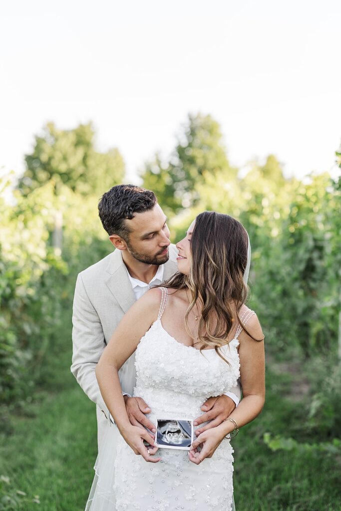 Bride and groom holding baby ultrasound during wedding portraits