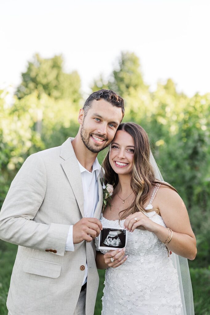 Bride and groom holding an ultrasound photo during their Bayview wedding at Gallagher Farms