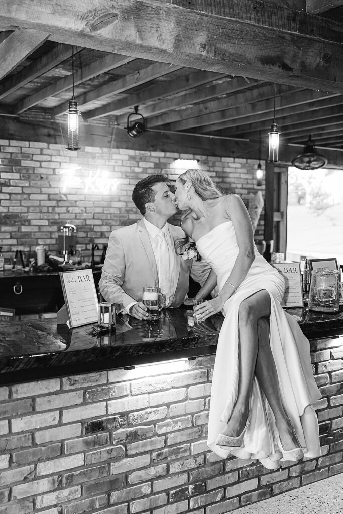 Bride and groom sitting at the bar during wedding portraits at Heritage Wedding Barns