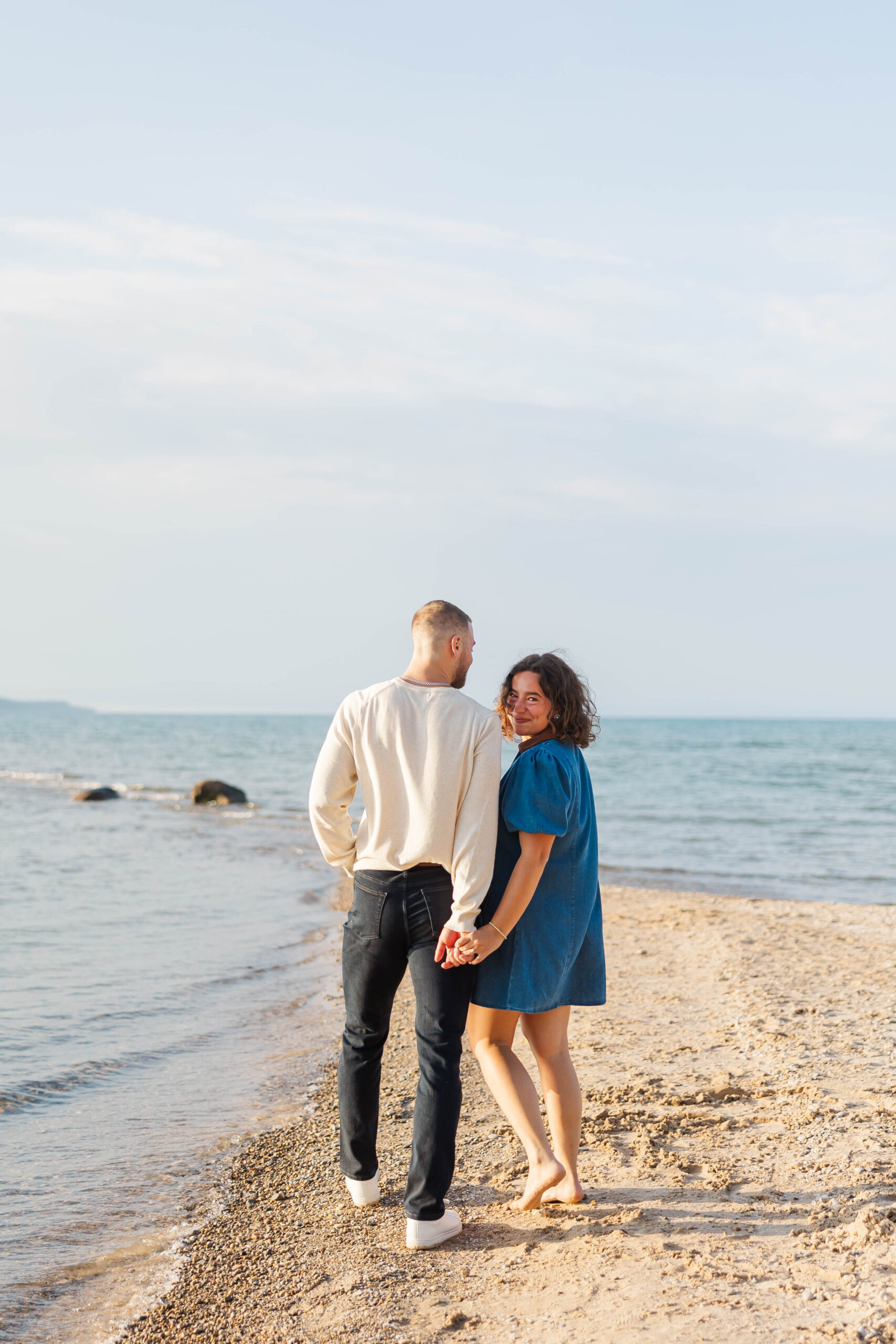 Jake and Brigitte walking hand in hand along the beach after their Elk Rapids proposal in Northern Michigan.