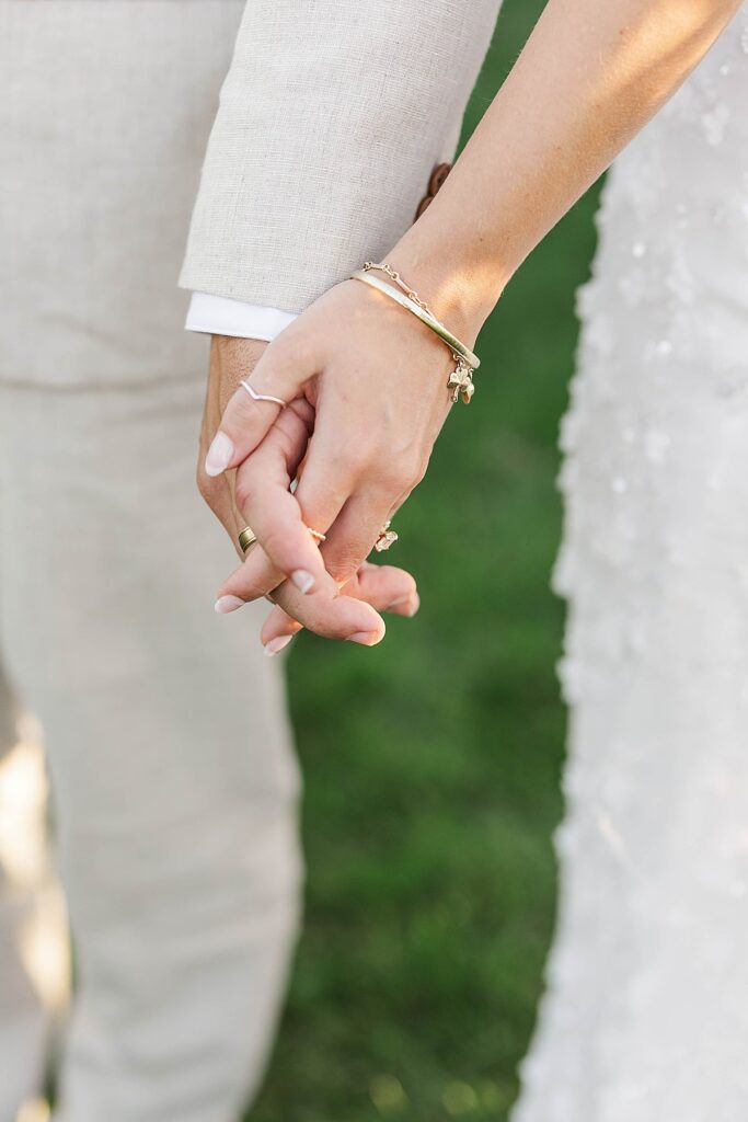 Bride and groom holding hands with wedding rings at Bayview Weddings at Gallagher Farms