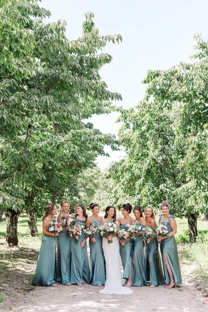 Bride and bridal party walking through orchard trees at Bayview Weddings at Gallagher Farms
