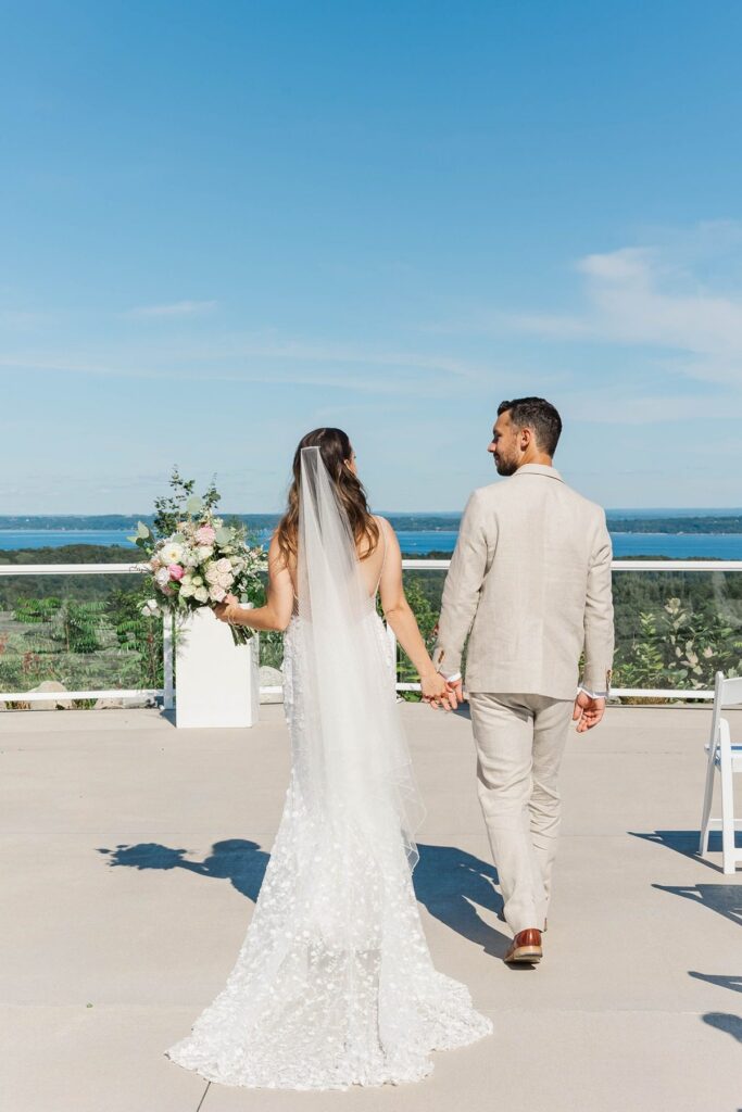 Bride and groom walking at the overlook ceremony site with florals at Bayview Weddings at Gallagher Farms in Northern Michigan