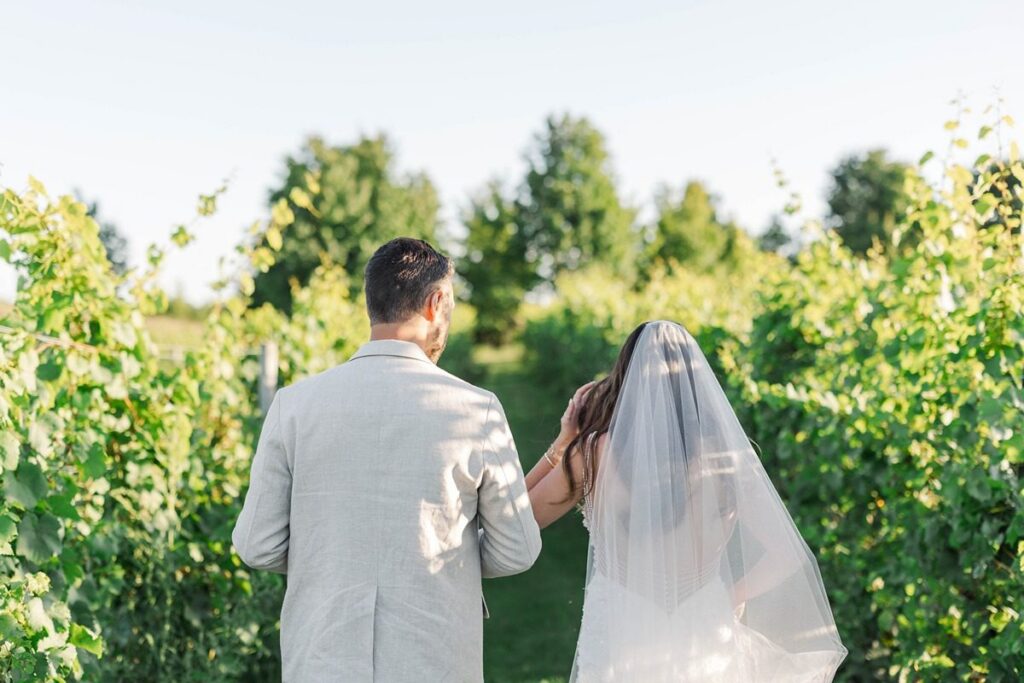 Bride and groom walking candidly through the vineyard with veil flowing in the wind during a summer wedding at Bayview Weddings at Gallagher Farms