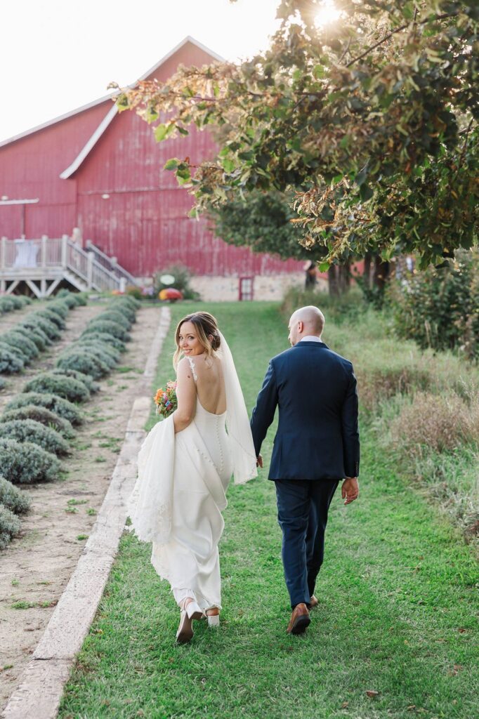 Bride looking back while walking with her groom through the lavender fields after their Lavender Hill Farm wedding ceremony