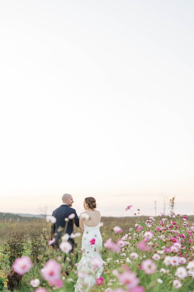 Bride and groom walking through the cosmos flower field at Lavender Hill Farm after their wedding ceremony