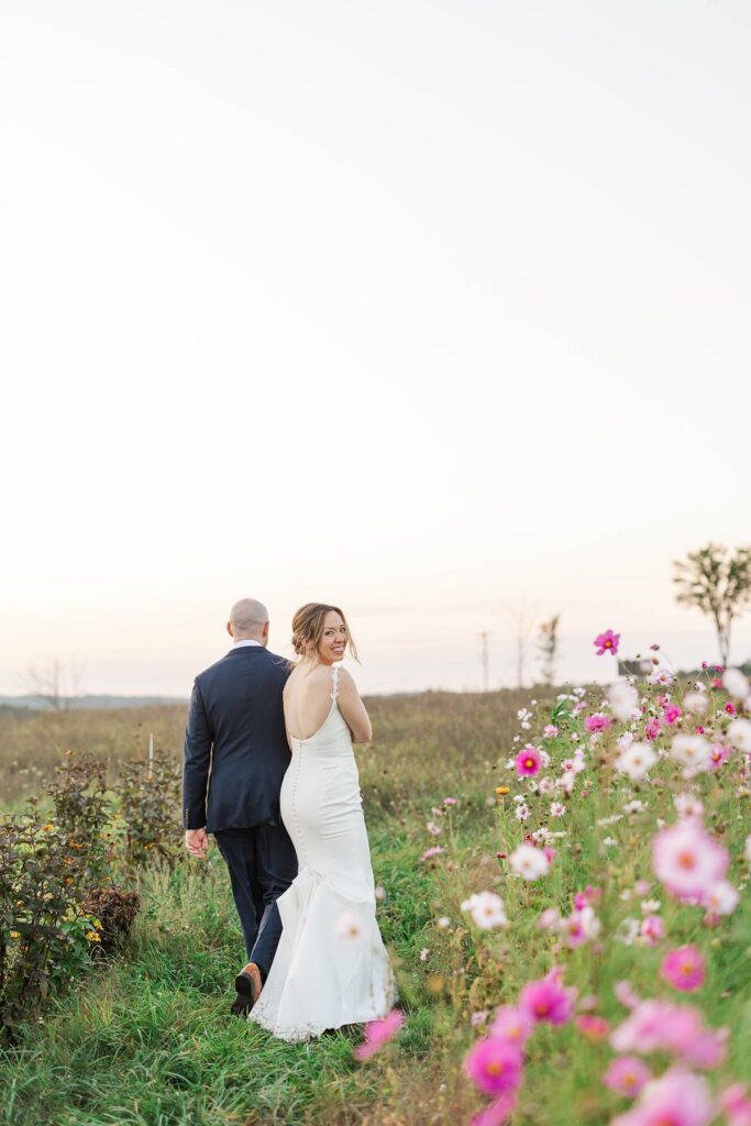 Bride looking back while walking through the cosmos flower field at Lavender Hill Farm