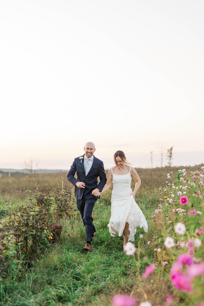 Bride and groom running through the cosmos flower field at Lavender Hill Farm