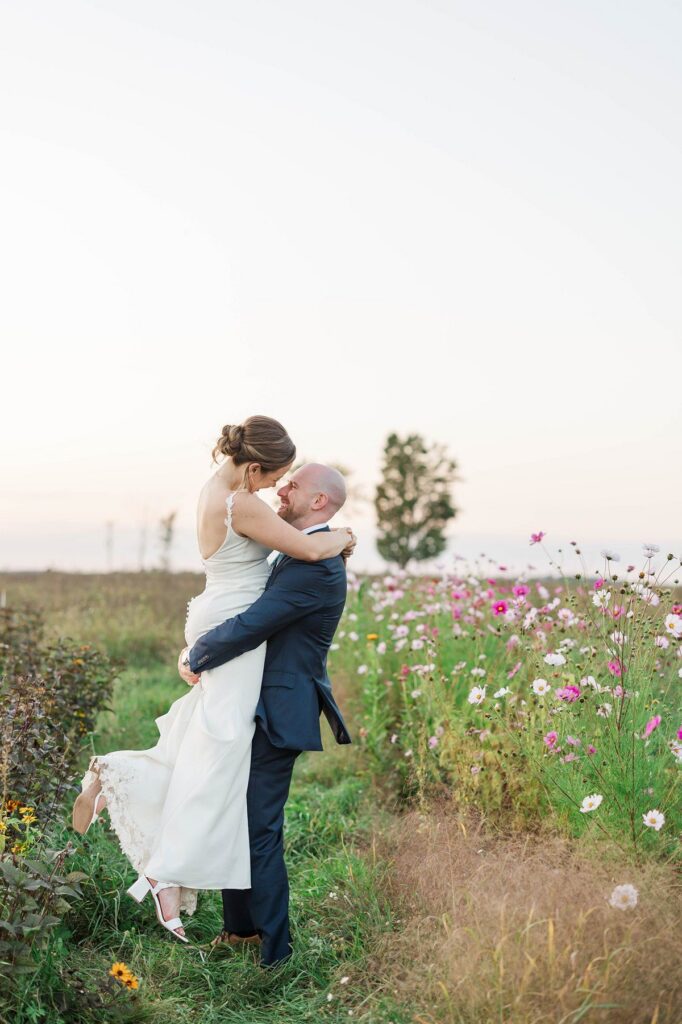 Groom lifting his bride in the cosmos flower field at Lavender Hill Farm