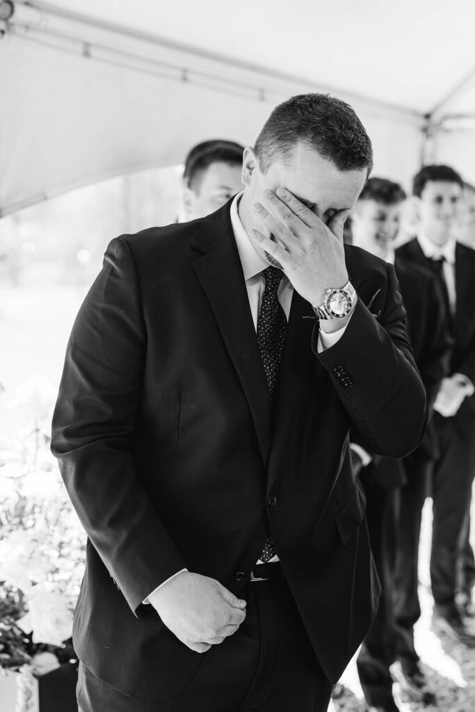 Groom wiping away tears as he watches his bride walk down the aisle during their emotional Mill Pond Event Center wedding ceremony.