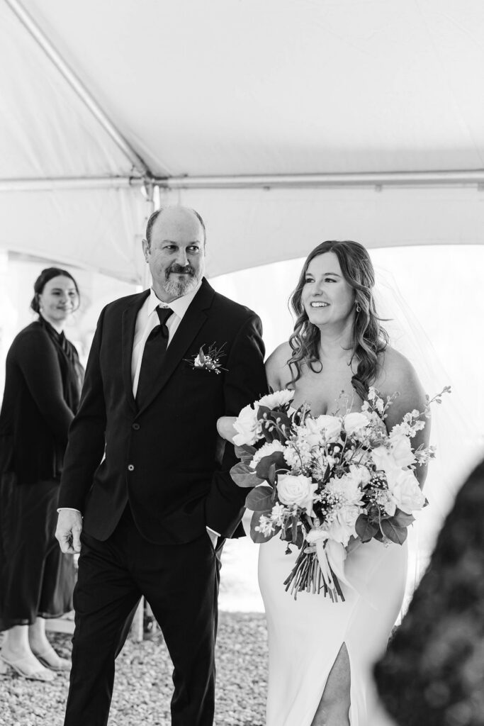 Madison smiling as she walks down the aisle with her dad during their Mill Pond Event Center wedding in Kalkaska, Michigan.
