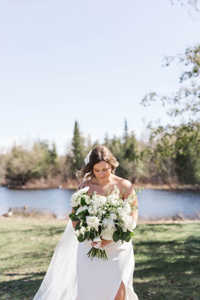 Bride Madison holding her white wedding bouquet during portraits at her Mill Pond Event Center wedding in Kalkaska, Michigan.