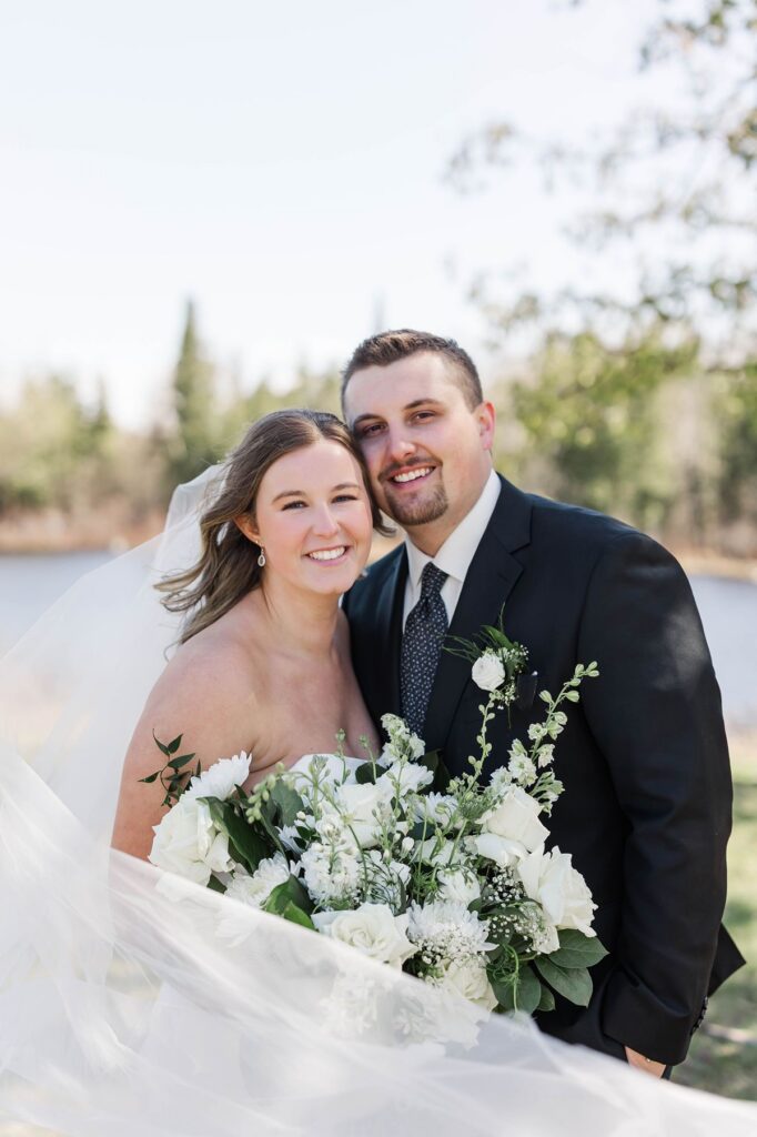 Madison and Jaxon smiling together during portraits at their Mill Pond Event Center wedding in Kalkaska, Michigan.