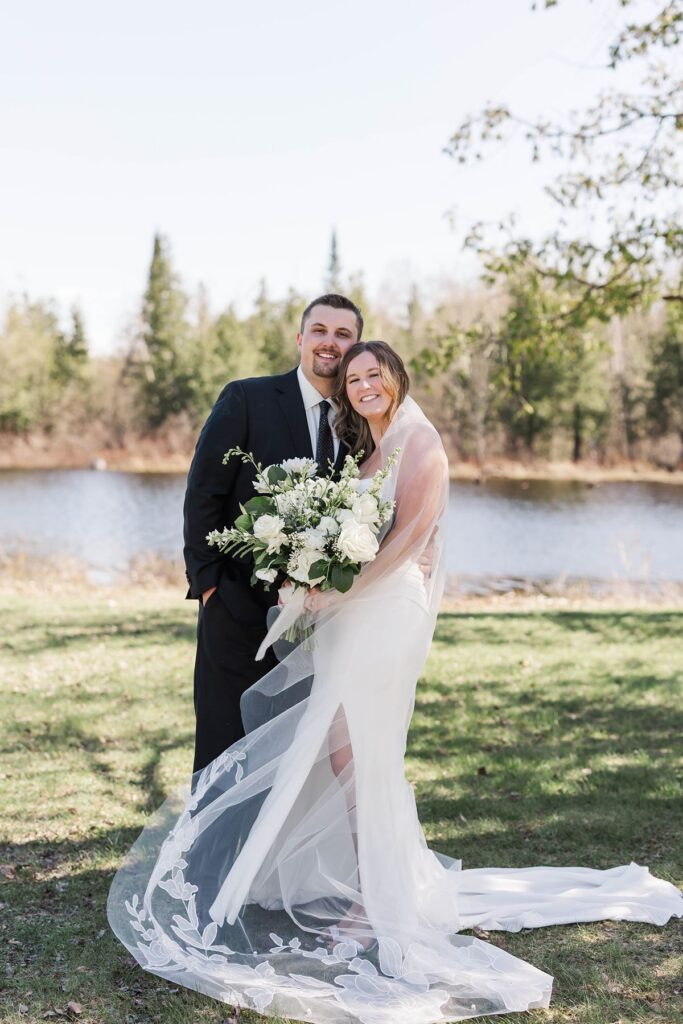 Madison and Jaxon smiling together during lakeside portraits at their Mill Pond Event Center wedding in Kalkaska, Michigan.