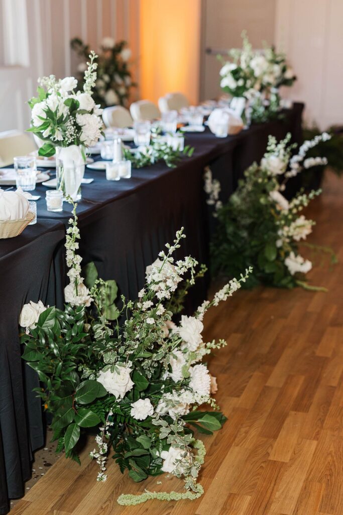 Elegant head table with lush white floral arrangements by Sunday Morning Flowers at Madison and Jaxon's Mill Pond Event Center wedding.