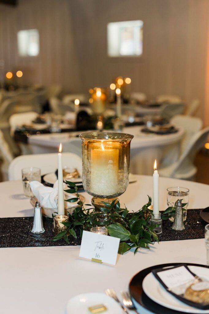 Elegant candlelit wedding reception table with greenery and timeless black and white decor at Mill Pond Event Center.