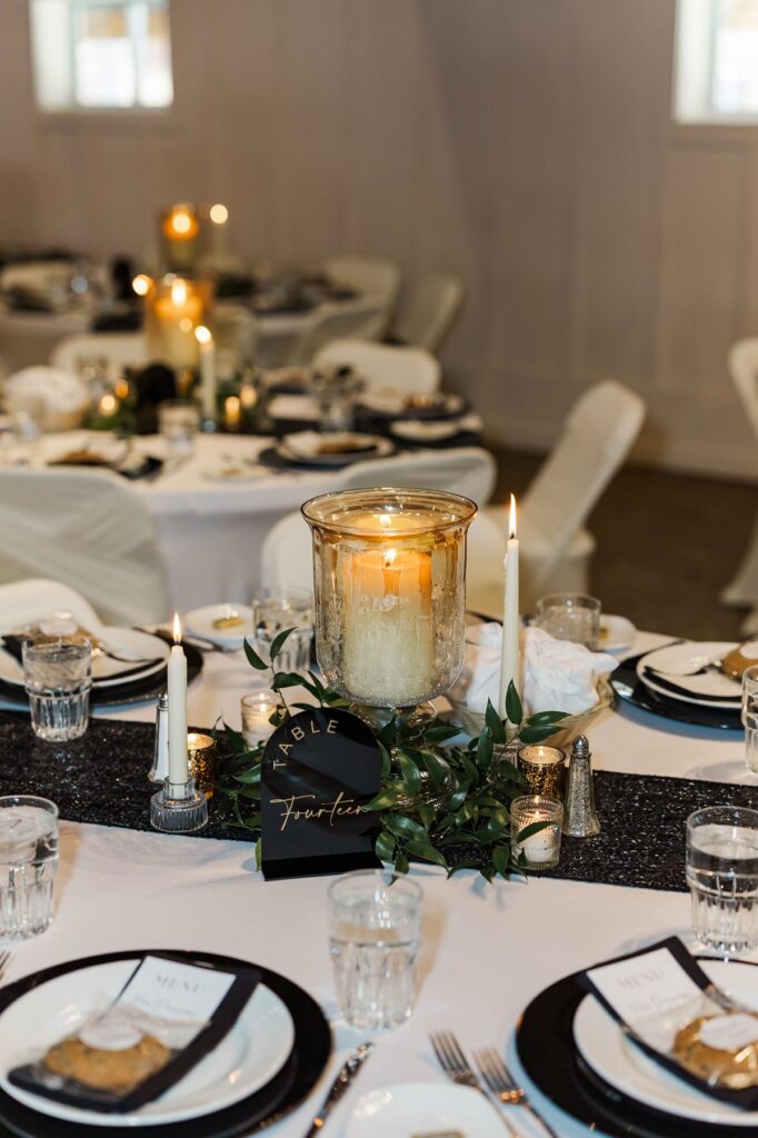 Candlelit reception tablescape with timeless black and white details and floral centerpieces by Sunday Morning Flowers at Mill Pond Event Center in Kalkaska, Michigan.