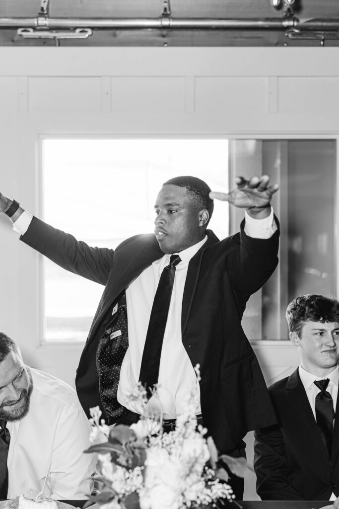 Groomsman celebrating during reception speeches at Madison and Jaxon's Mill Pond Event Center wedding in Kalkaska, Michigan.