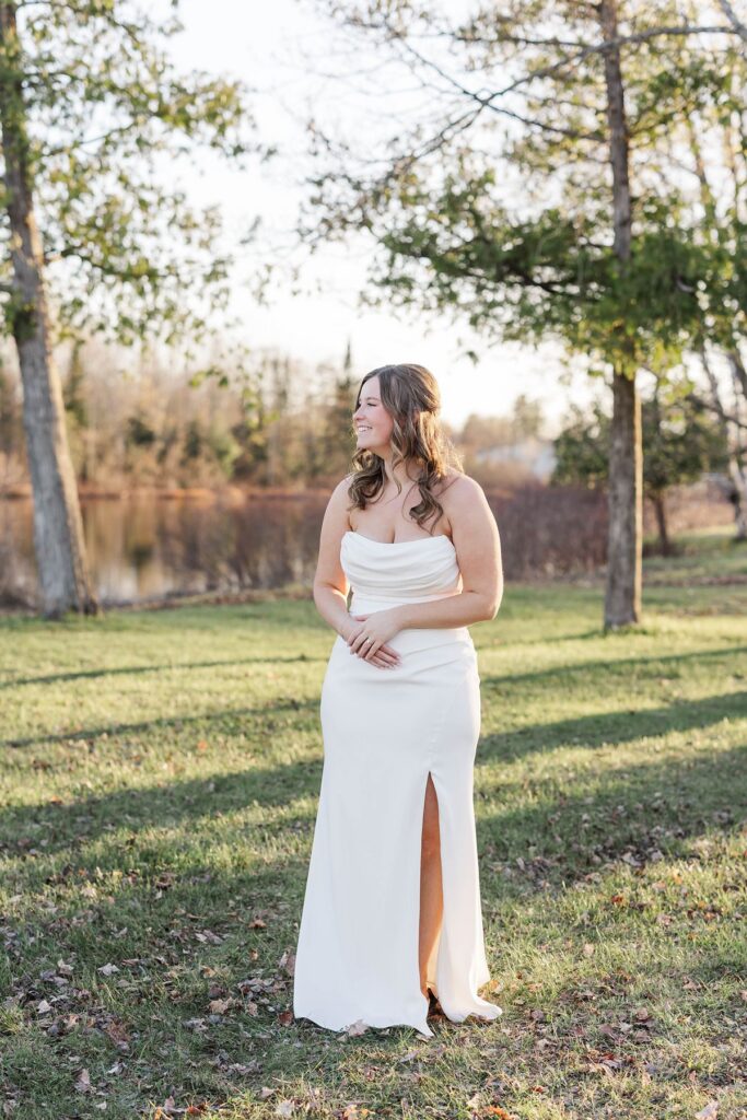 Bride Madison smiling during bridal portraits by the lake at her Mill Pond Event Center wedding in Kalkaska, Michigan.