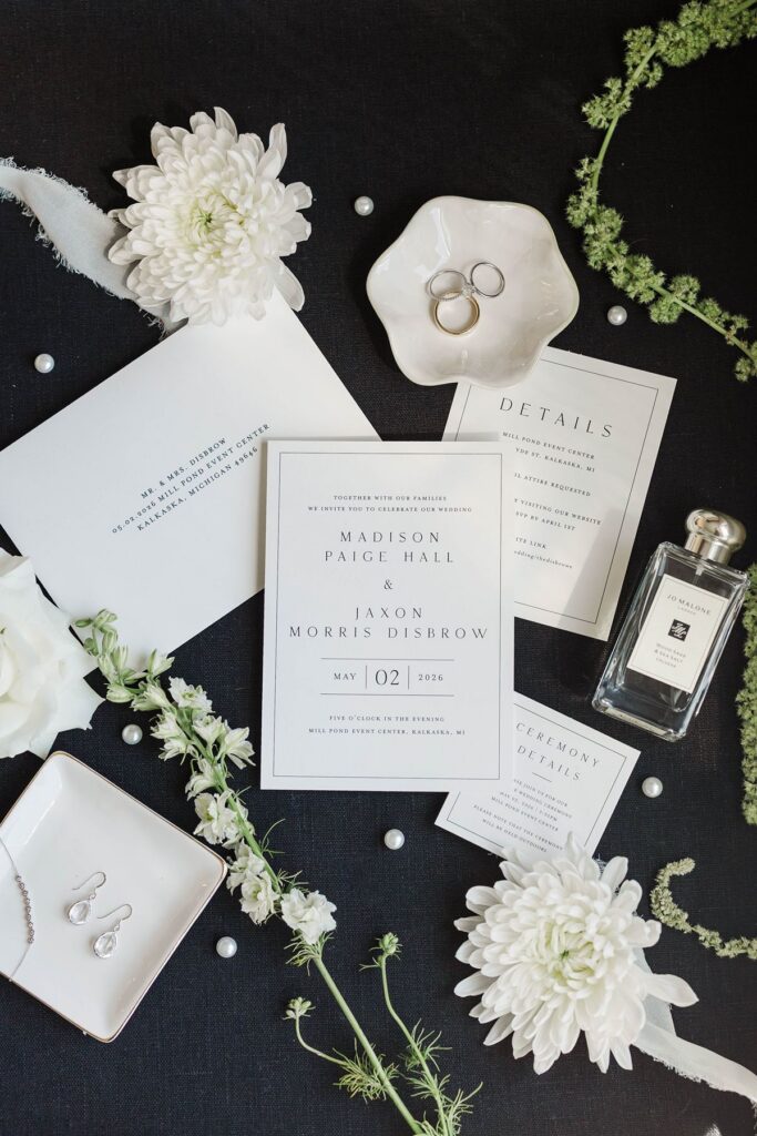 Bridal details including invitations, rings, perfume, and white florals for Madison and Jaxon's Mill Pond Event Center wedding.