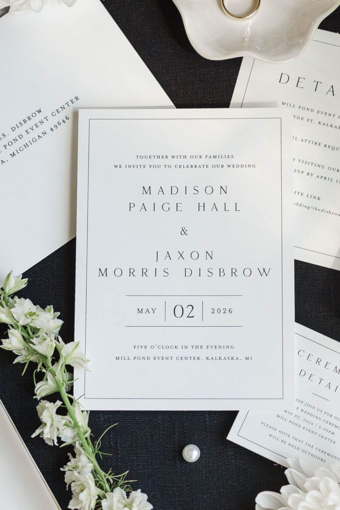 Wedding invitation suite with rings, shoes, jewelry, and white florals styled for Madison and Jaxon's Mill Pond Event Center wedding.