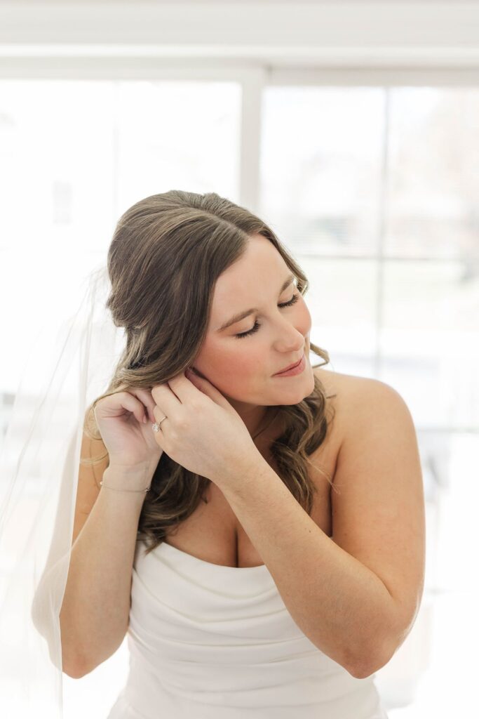 Bride putting on her earrings while getting ready before her Northern Michigan wedding at Mill Pond Event Center.