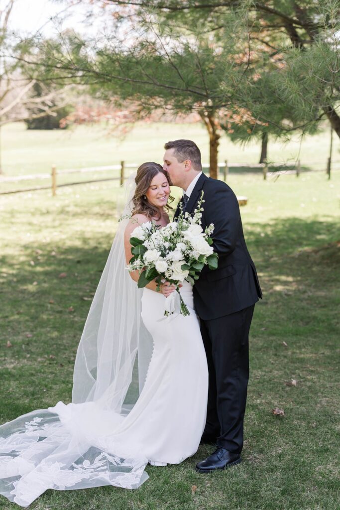 Groom kissing the bride's forehead during romantic portraits at their Mill Pond Event Center wedding in Northern Michigan.